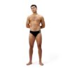 גבר במדים של Speedo עם ביקיני שחור, עומד מול רקע לבן.