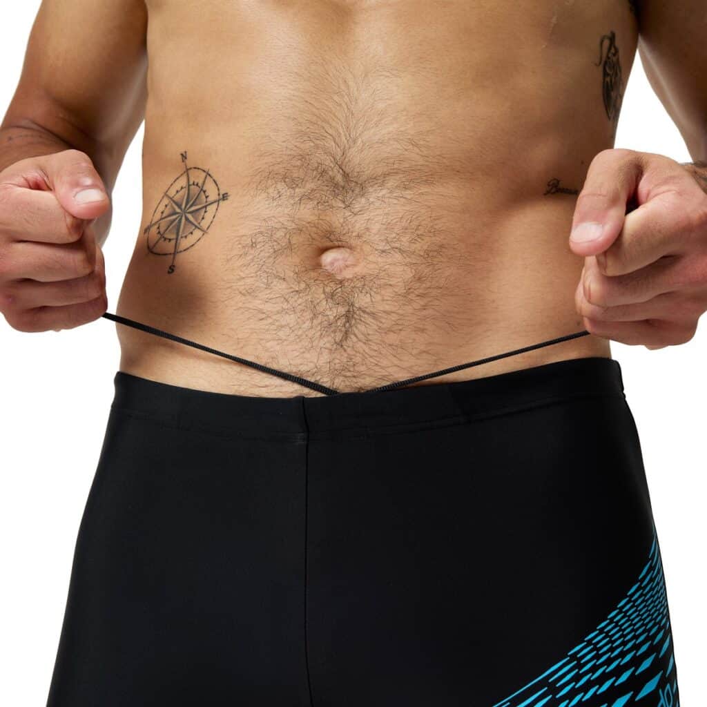 קוד כותרת תמונה: בגדי ים Speedo לגבר גבר במדים של Speedo מושך את חוט המותג, לבוש בבגדי ים שחורים.