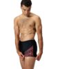 גבר לובש בגד ים שחור של Speedo עם דוגמה אדומה, מוכן לשחייה.