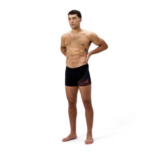 גבר מודרני לובש בגד ים שחייה של Speedo, עומד על רקע לבן.